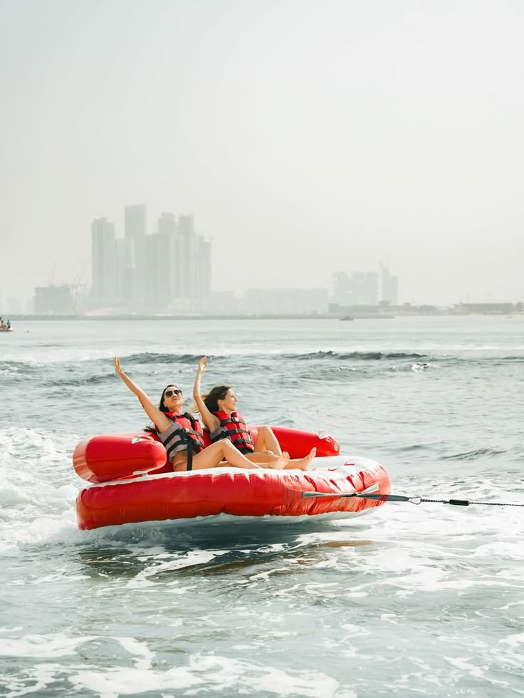 Two people enjoy tubing on water with city skyline in background.