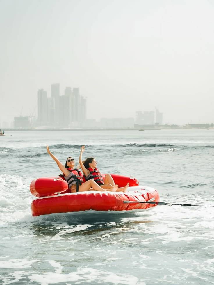 Two people enjoy tubing on water with city skyline in background.