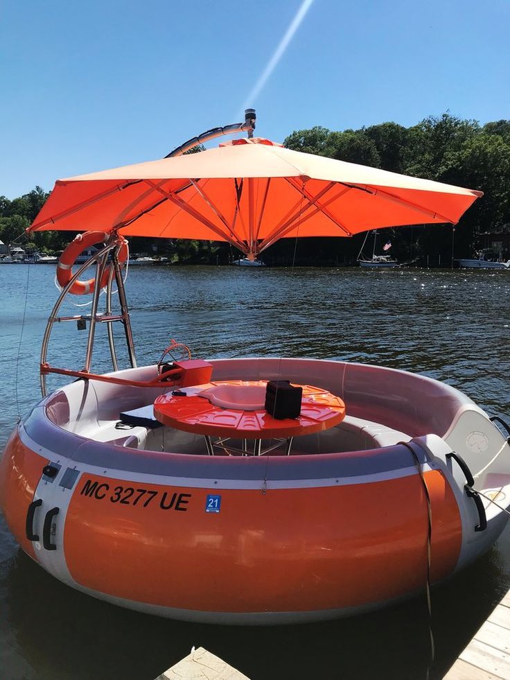 Floating orange boat with a matching umbrella on a sunny day by the water.