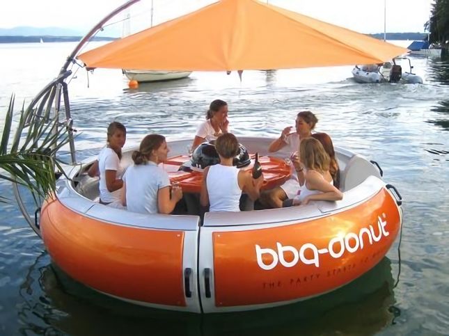 Group of people sitting in a floating, round orange boat with a canopy on a lake.