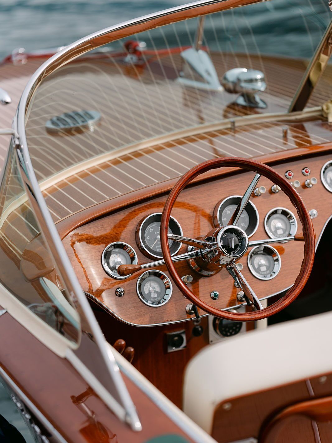 Vintage wooden boat dashboard with steering wheel and gauges.