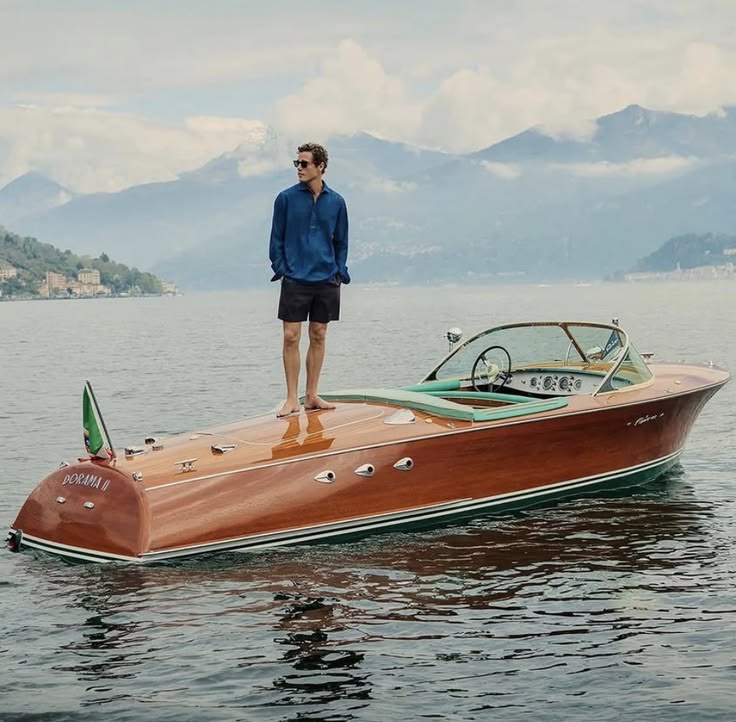 Person standing on a vintage wooden speedboat on a lake.