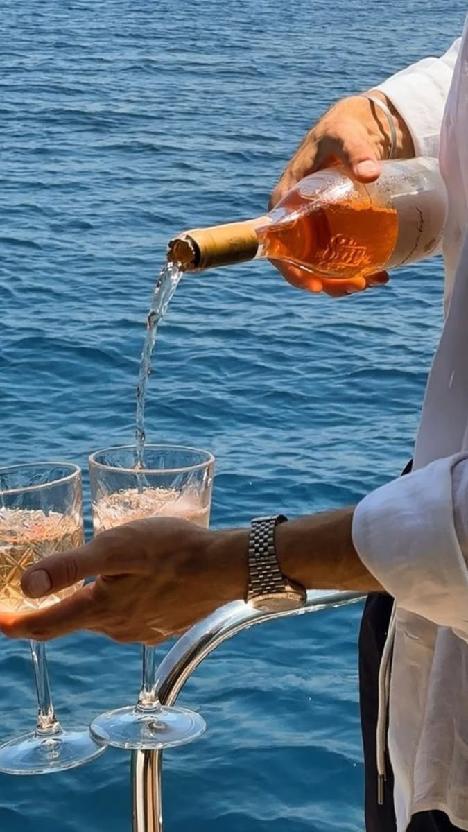 Person pouring rosé wine into glasses on a boat.